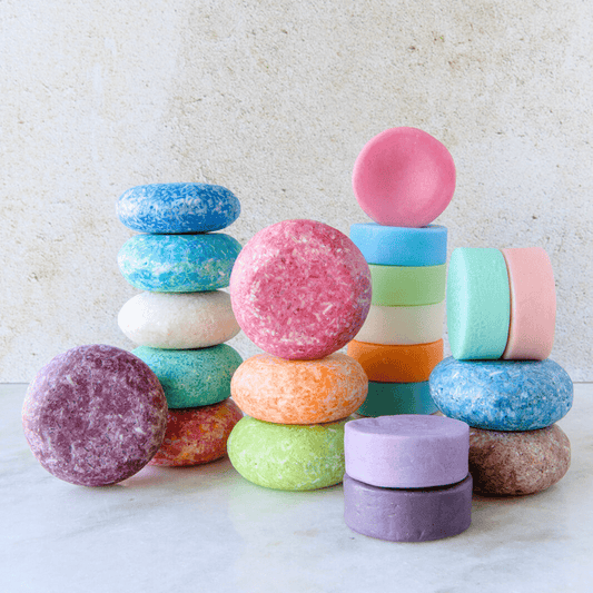 Shampoo & Conditioner Bar Duo by ZeroWasteStore.com features colorful, round zero waste bars stacked on a light surface. The bars come in bright shades like blue, pink, purple, green, and orange against a neutral background.