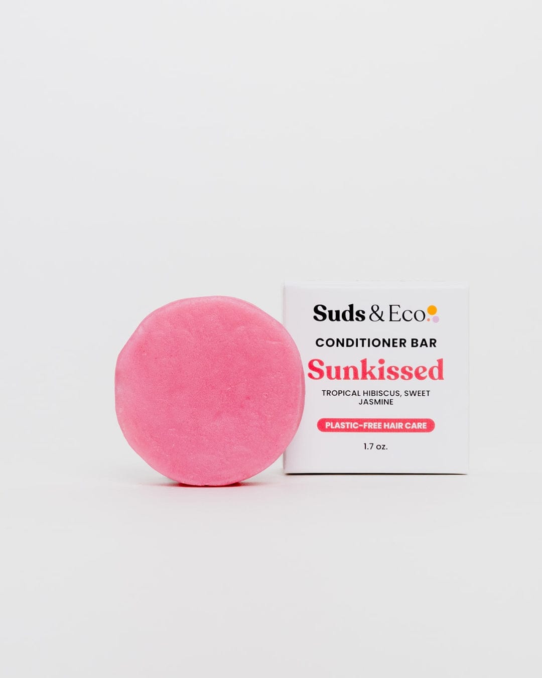 A round, pink Conditioner Bar from ZeroWasteStore.com sits by a white box. The Sunkissed bar features tropical hibiscus and sweet jasmine. It’s sulfate-free and plastic-free, offering an eco-friendly hair care option.