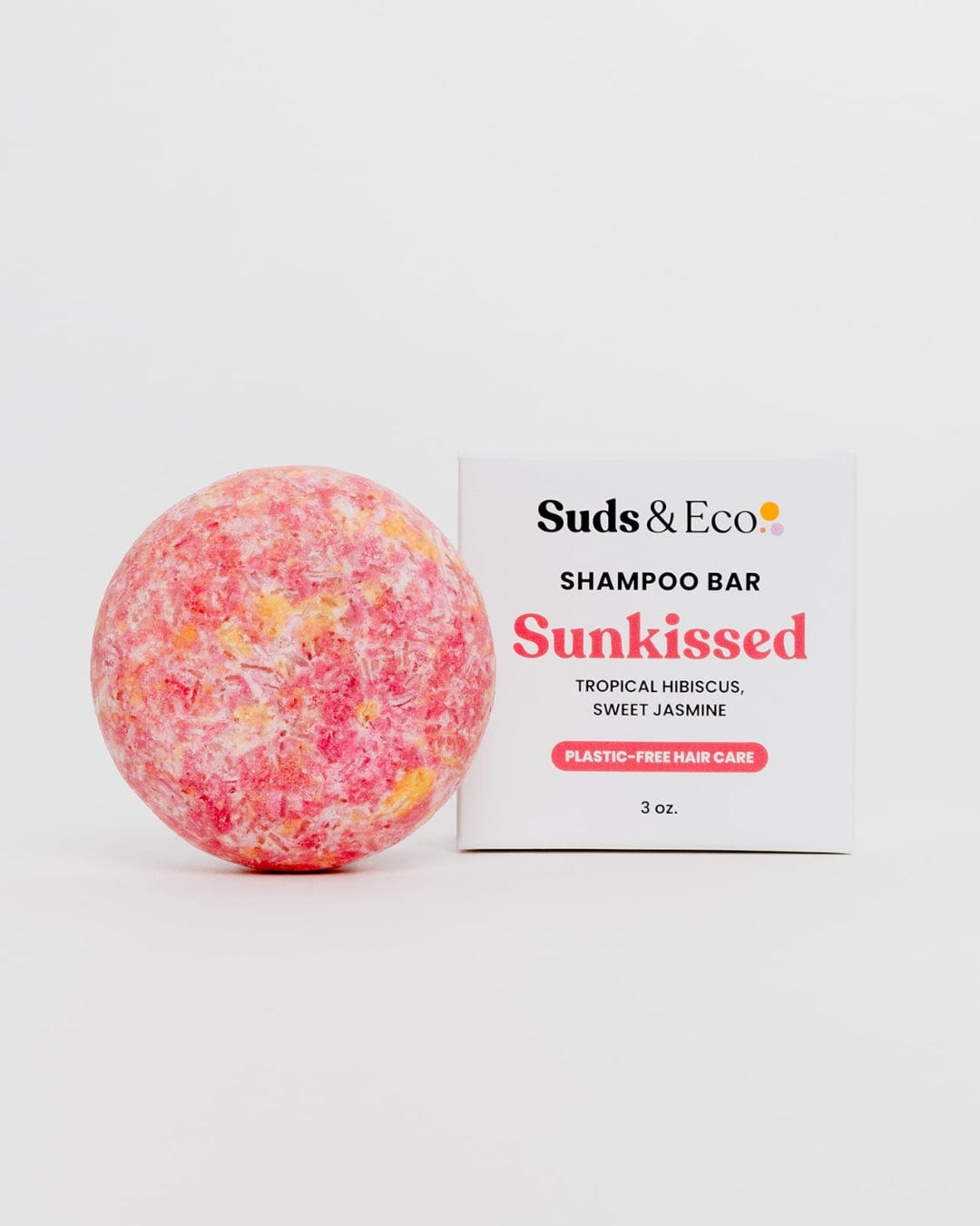 A round, pink and yellow Shampoo Bar from ZeroWasteStore.com sits by its box on a white background. This vegan, zero-waste bar features tropical hibiscus and sweet jasmine scents and weighs 3 oz. Plastic-free hair care at its finest.