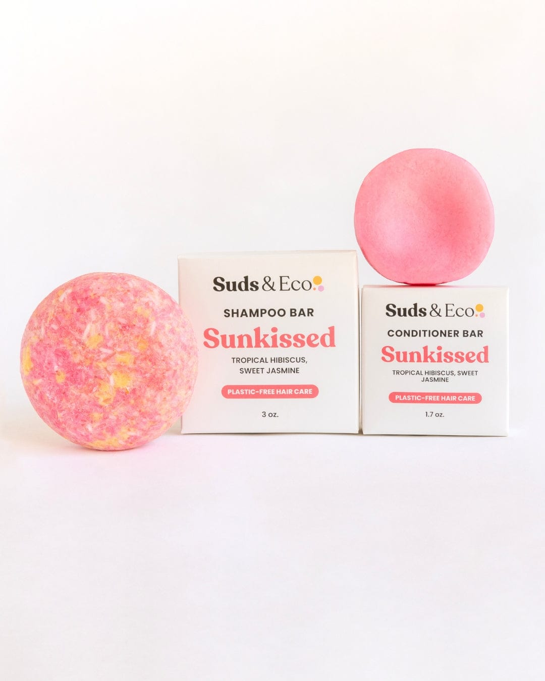 Two round pink Shampoo & Conditioner Bar Duo bars from ZeroWasteStore.com—one textured, one smooth—are shown with branded boxes. Sunkissed offers tropical hibiscus & sweet jasmine scents for a zero waste hair care routine.