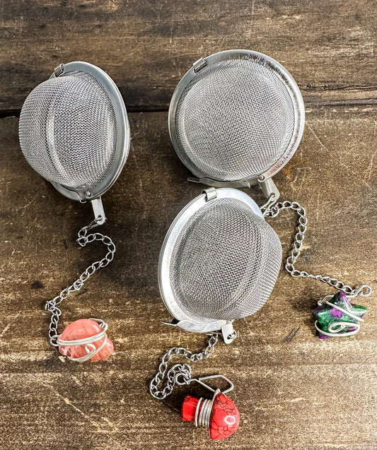 Herbalroseapothecary tea ball infuser with stainless steel mesh ball for loose leaf tea brewing, hanging on a white background.