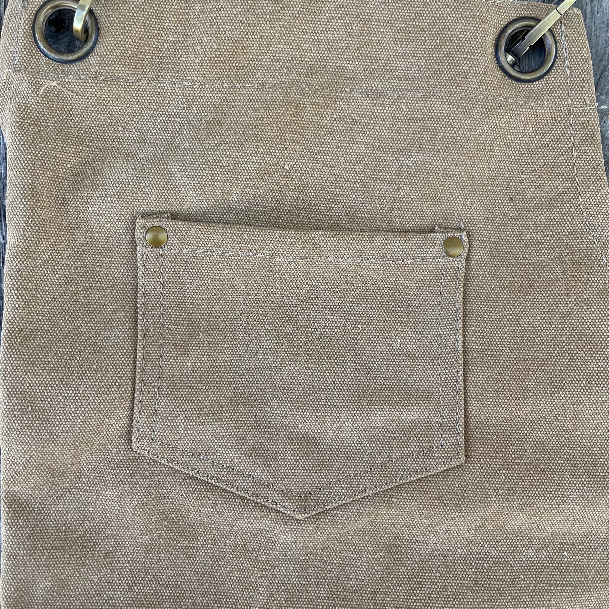 The Celtic Farm Gardening Apron - Waxed Canvas Apron with Pockets features a small front pocket, metal rivets at the corners, and large metal grommets at the top for durability.