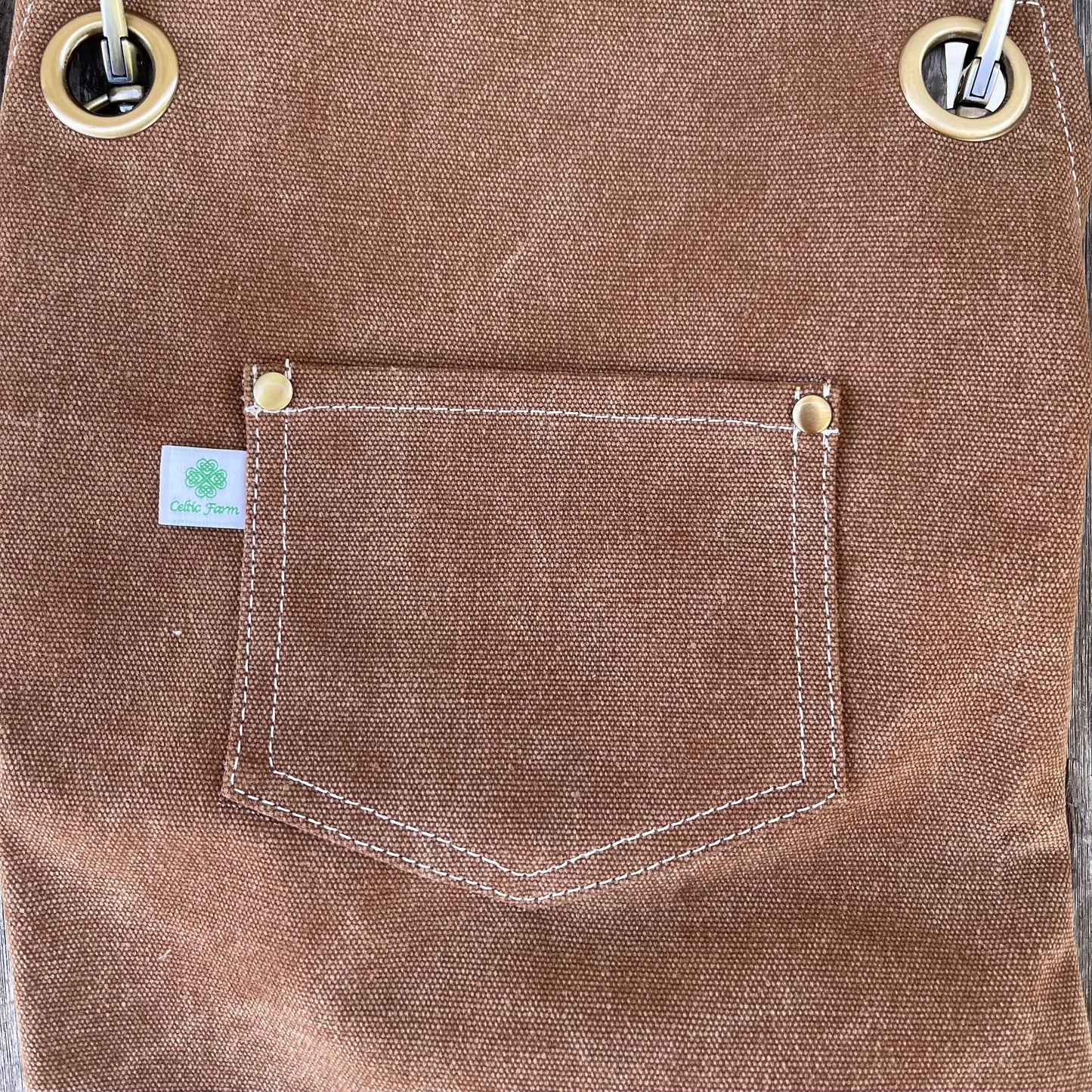 Close-up of a brown waxed cotton canvas pocket with white stitching and metal rivets on The Celtic Farm Gardening Apron - Waxed Canvas Apron with Pockets; features a green and white label—perfect for gardeners or florists.
