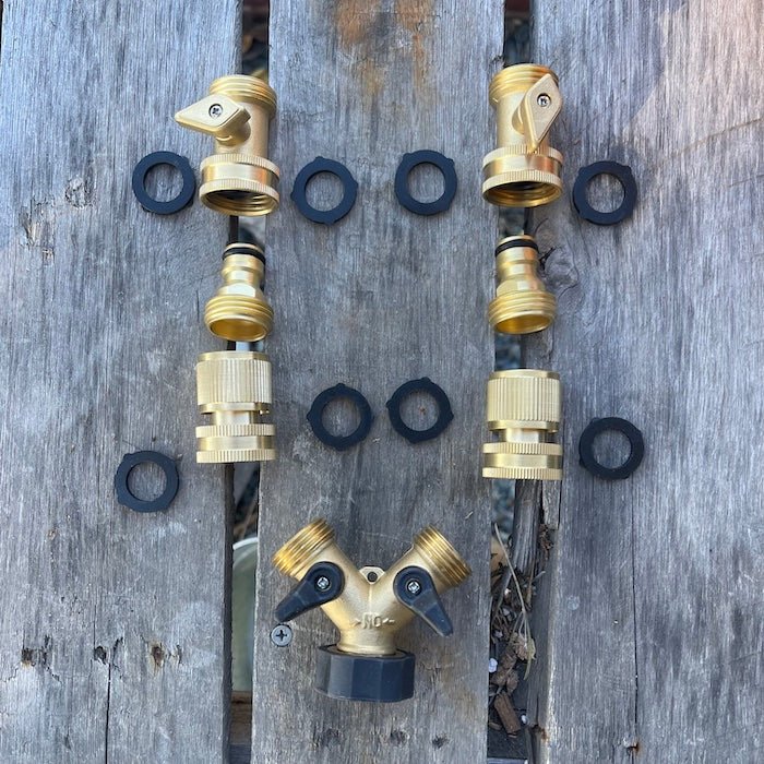 The Celtic Farms Brass Hose Organization Bundle is displayed on wood, with connectors and black rubber washers arranged as a smiley face, showcasing their reliable, leak-proof design for organizing your garden hose.