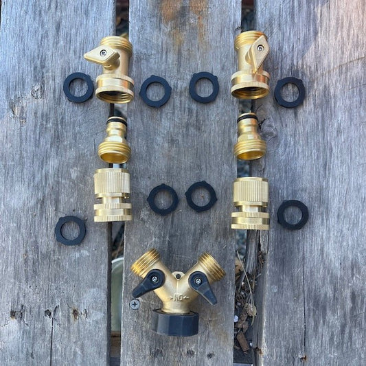 The Celtic Farms Brass Hose Organization Bundle is displayed on wood, with connectors and black rubber washers arranged as a smiley face, showcasing their reliable, leak-proof design for organizing your garden hose.