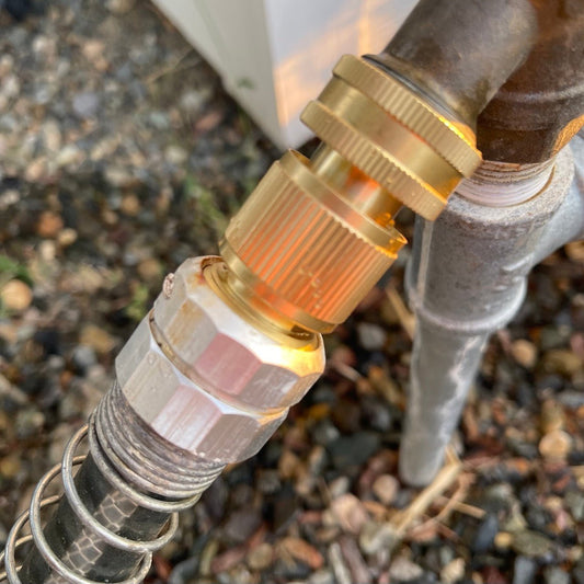 A close-up of The Celtic Farm Brass Hose Organization Bundle, showing its brass connectors and leak-proof connection attached to an outdoor spigot, with gravel visible in the background.