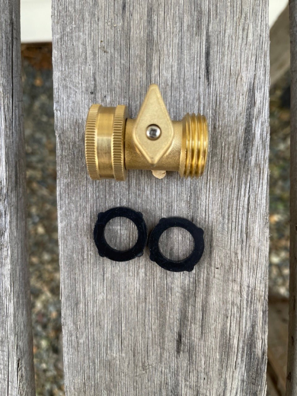 The Celtic Farm’s Brass Hose Organization Bundle, including a brass shut-off valve and two black rubber washers, sits on a weathered wooden surface ensuring a leak-proof connection for your garden hose.