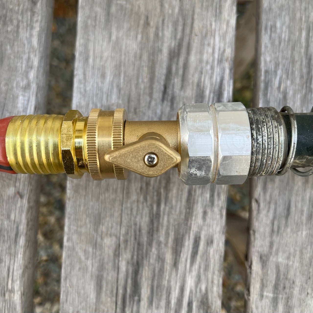 Close-up of The Celtic Farm Brass Hose Organization Bundle, featuring brass connectors between hoses on a weathered wood surface for a leak-proof connection. Organize your garden hose with reliable metal fittings.
