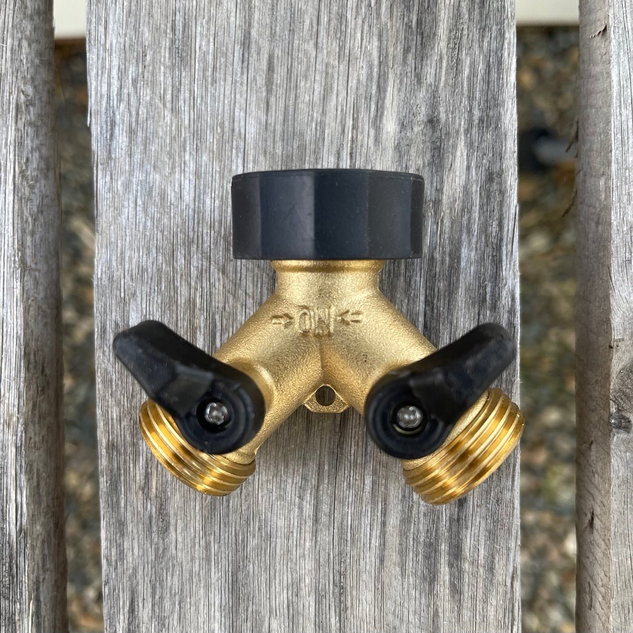 The Celtic Farm Brass Hose Organization Bundle: a Y-shaped brass splitter with two black shut-off valves and leak-proof connection, shown on a gray wooden surface. Ideal for use with brass garden connectors or any hose organization kit.