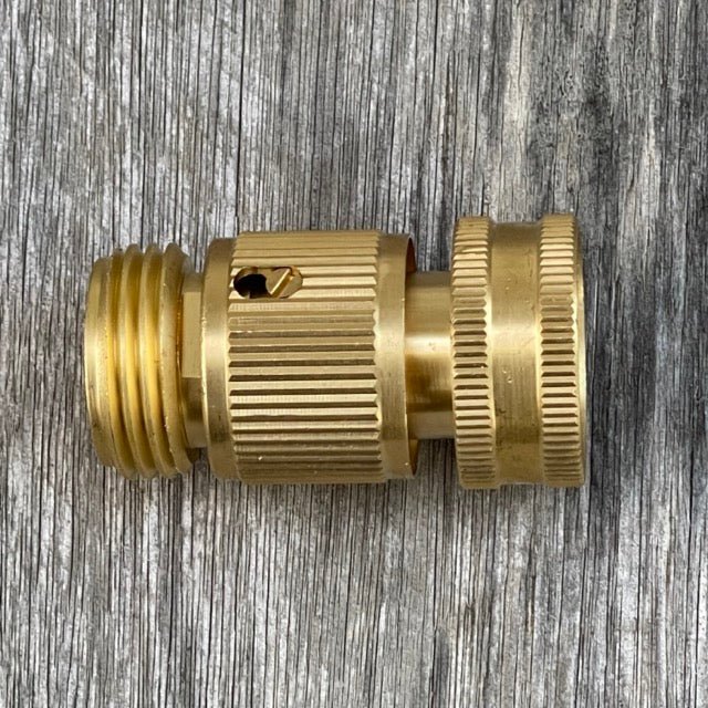 The Celtic Farm Garden Hose Brass Quick Connect Connector, featuring ridged grips, lies horizontally on a weathered wooden surface, providing fast connect/disconnect for a leak-proof connection.