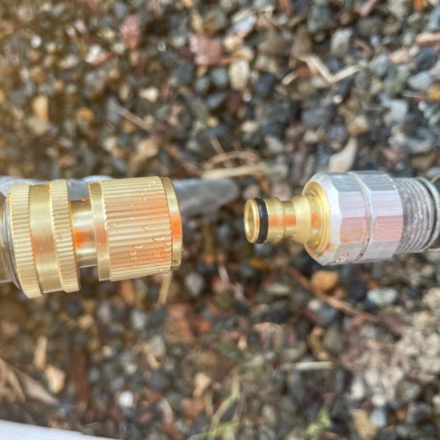 Close-up of The Celtic Farm Garden Hose Brass Quick Connect Connectors, positioned on small rocks and soil, with ends aligned for easy joining.