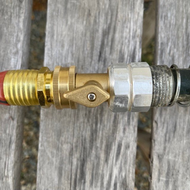 Close-up of The Celtic Farm Garden Hose Brass Shutoff Valve creating a leak-proof connection between a red and a green garden hose on a wooden surface.
