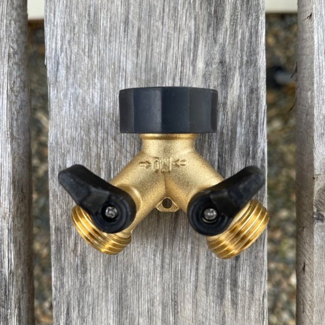 The Celtic Farm Two-way Brass Garden Hose Splitter features a Y-shape with two black handles, offering a secure, leak-proof connection for garden hoses and is pictured on a weathered wooden surface.