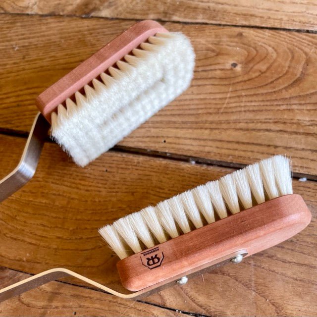 Two Indoor Plant Dust Brushes by The Celtic Farm, crafted from pearwood and goat hair with white bristles and metal handles, rest on wood. Ideal for gentle cleaning or scrubbing—these brushes make a unique gift for houseplant care.
