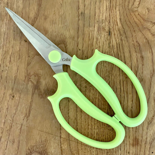 A pair of Floral & Herb Snips by The Celtic Farm, with light green handles, rests on a wooden surface. The slightly open blades are ideal for precise floral arranging and herb trimming tasks.