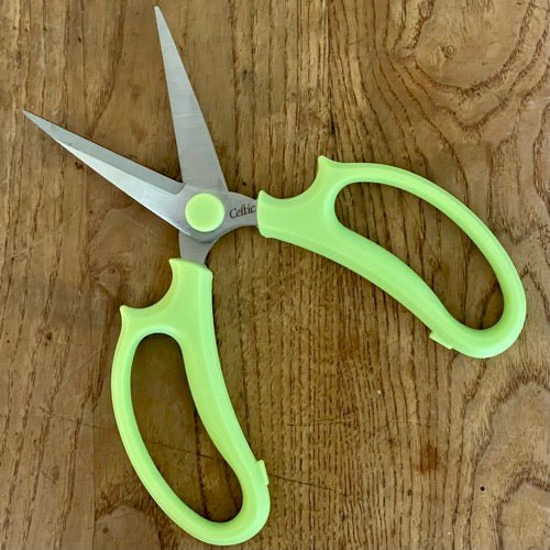 The Celtic Farm’s Floral & Herb Snips - Our Multipurpose Scissors, with light green handles and stainless steel blades, rest open on a wooden surface, ideal for precise floral arranging.
