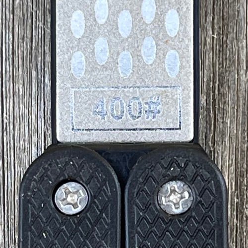 Close-up of The Celtic Farm Garden Tool Sharpener—Diamond + Carbon Steel Hone Reversible Paddle, featuring a 400# label, textured grip handles, and two screws on a wooden surface; perfect for sharpening pruners, clippers, mower blades, and scissors.