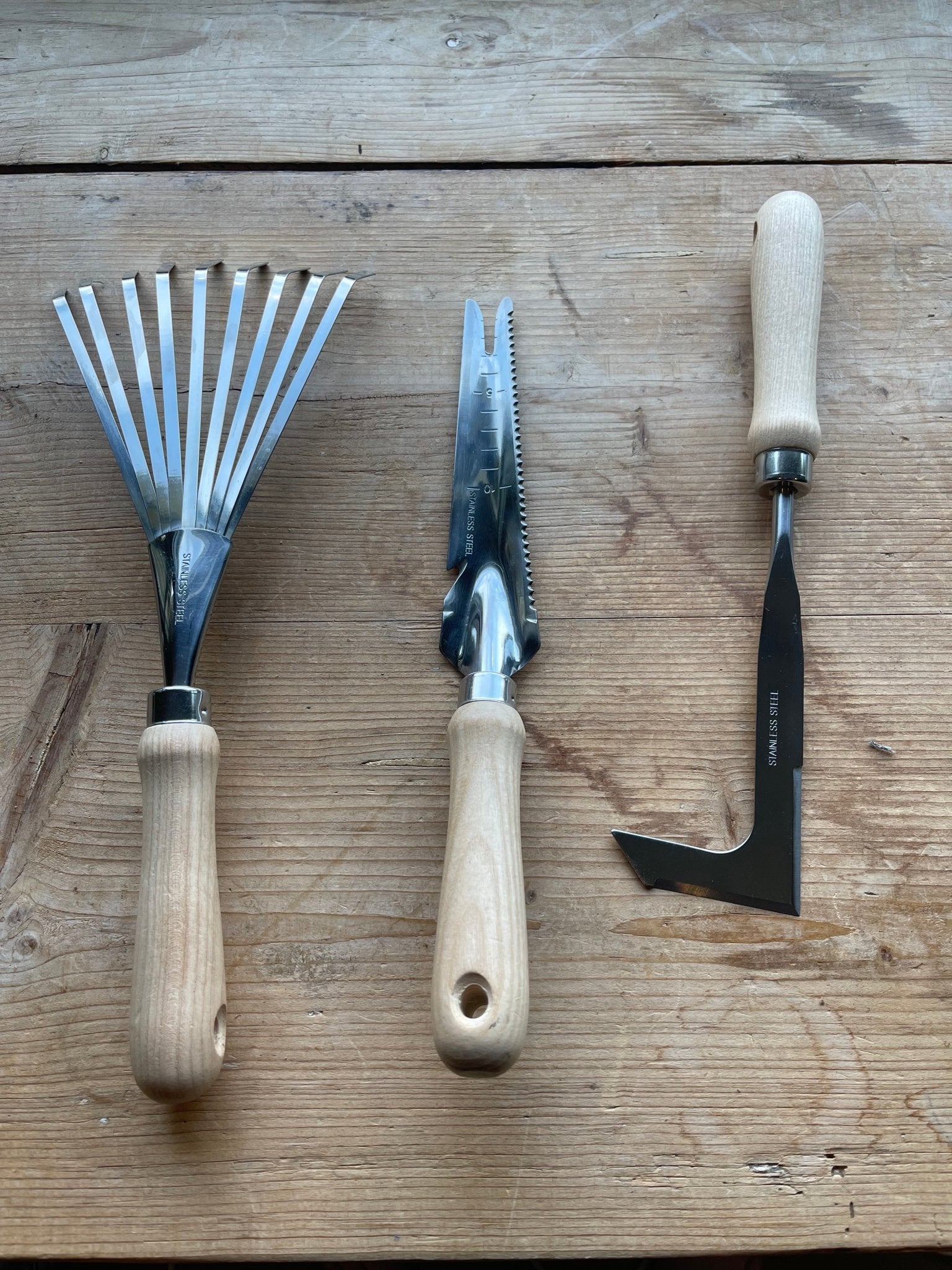 The Celtic Farm’s Unique Garden Tool Set & Gift features a hand rake, hori hori knife, and weeding tool with wooden handles, displayed side by side to highlight their quality craftsmanship and distinctive design.