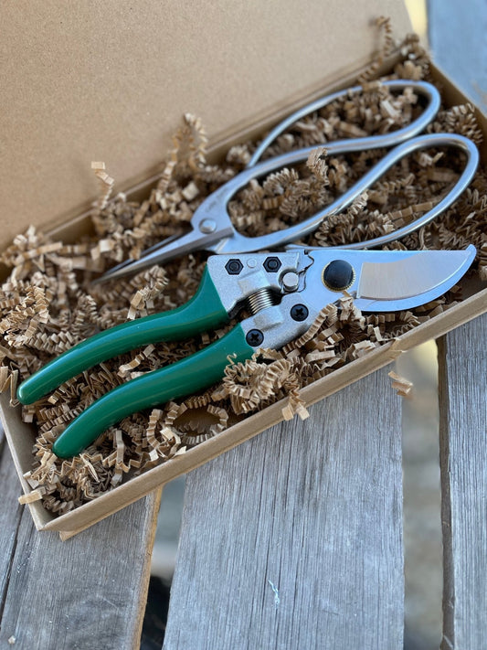 The Celtic Farm Garden Gift Box - Pruners and Snips features green-handled tools nestled in brown crinkle paper, elegantly presented on a rustic wooden surface.