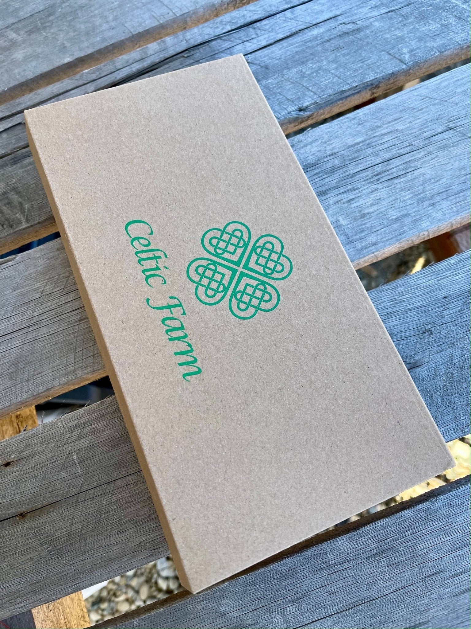 A rectangular brown cardboard Garden Gift Box - Pruners and Snips by The Celtic Farm, featuring green Celtic Jam text and a Celtic knot design, rests on a weathered wooden surface.