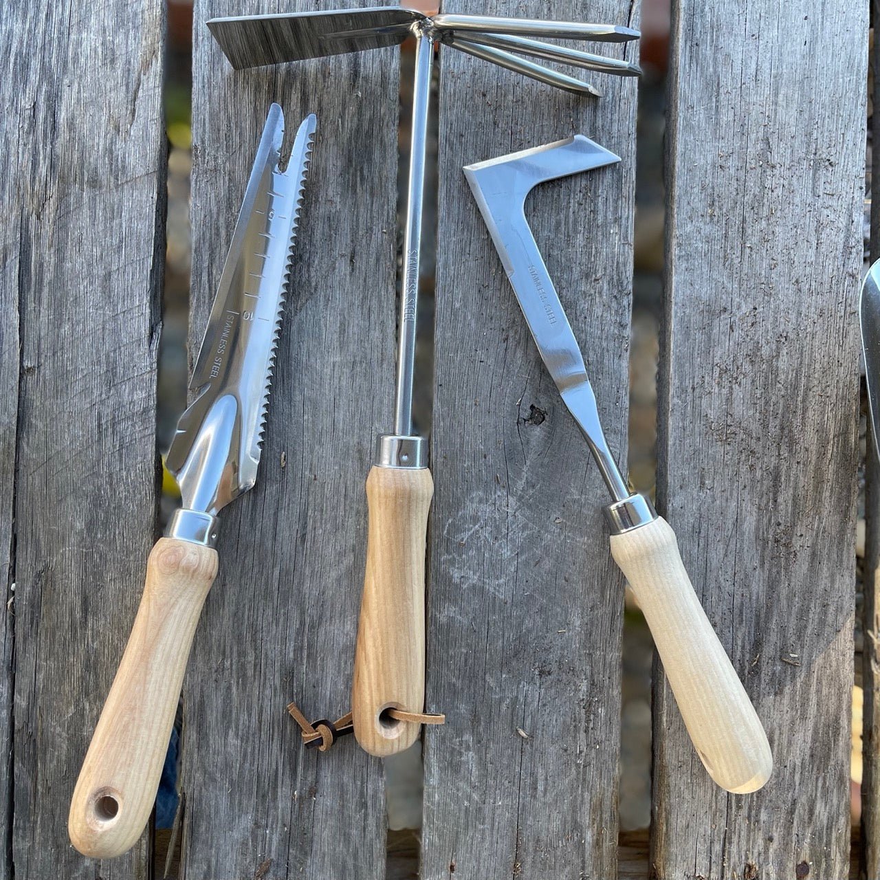 The Celtic Farms Unique Garden Tool Set & Gift Two features three essential garden tools with light wooden handles—a soil knife, hand cultivator, and hori-hori weeder—perfectly arranged on a rustic surface for every gardener.