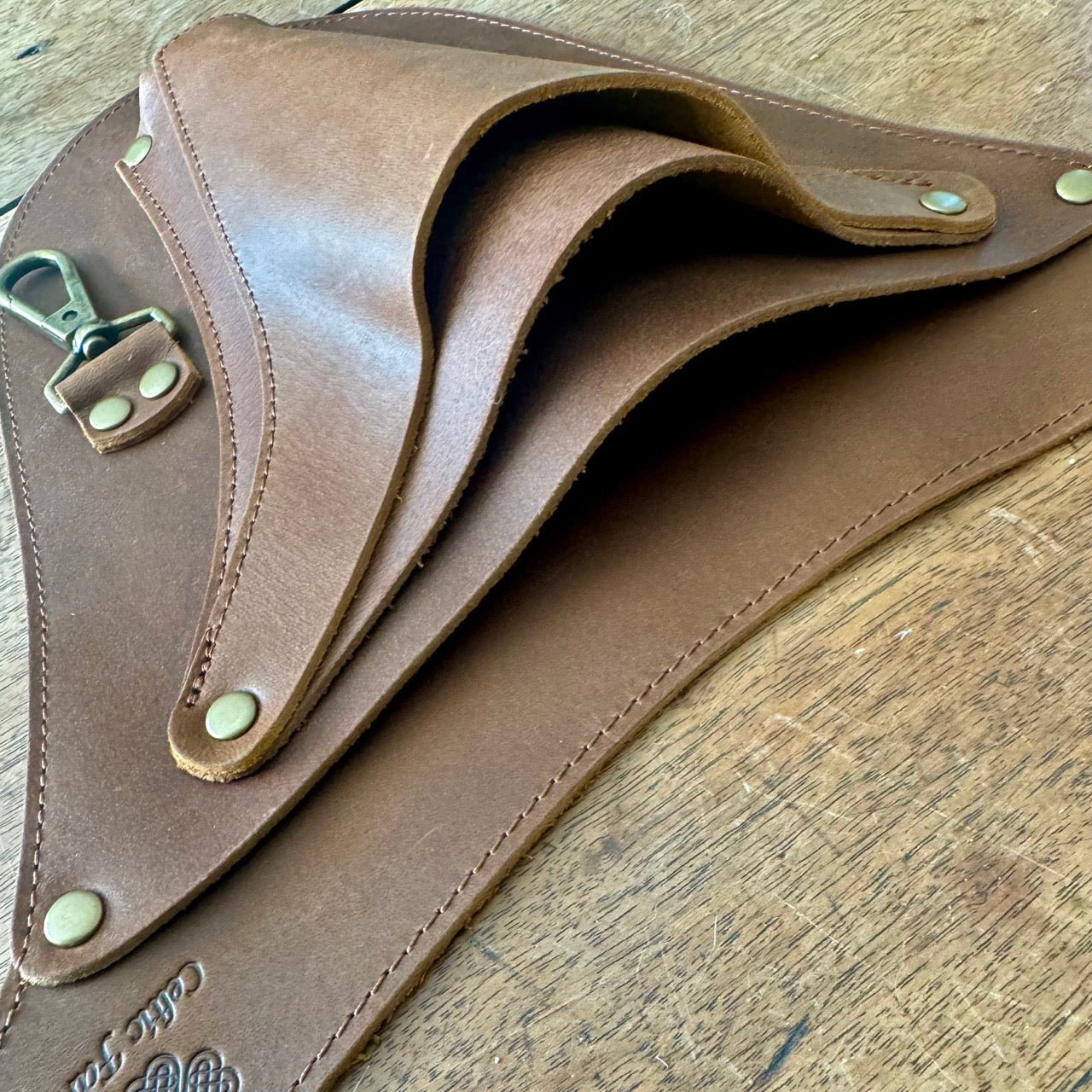 A close-up of The Celtic Farm’s Ultimate Leather Garden Tool Belt & Holder, featuring extra rivet reinforcement, a metal clasp, and visible stitching—expertly handcrafted for master gardeners to organize tools on a wooden surface.