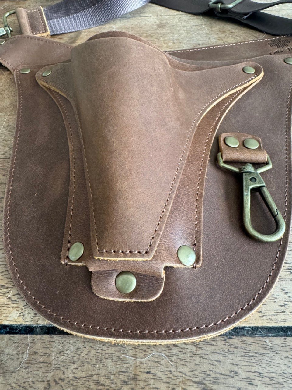 A close-up of The Celtic Farms Ultimate Leather Garden Tool Belt & Holder shows extra rivet reinforcement, detailed stitching, and a secure metal clip—master gardener designed for carrying tools on any gardening task.