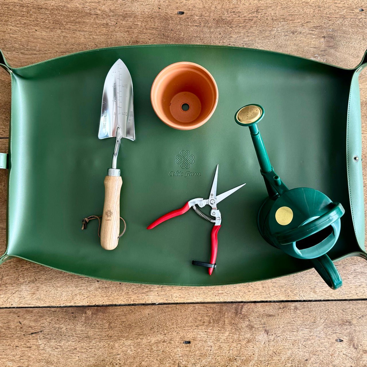 The Celtic Farm’s Potting Mat – Waterproof For Tidy Gardening keeps your trowel, terracotta pot, red-handled shears, and green watering can organized and compactly stored on any surface.
