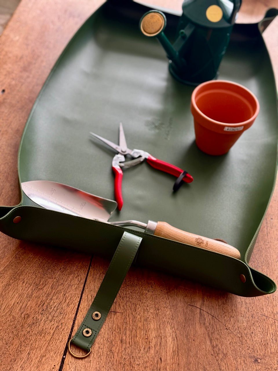 The Celtic Farm Potting Mat - Waterproof For Tidy Gardening sits on a table with gardening tools and a pot, perfect for compact storage and use indoors or outdoors as a convenient potting mat.