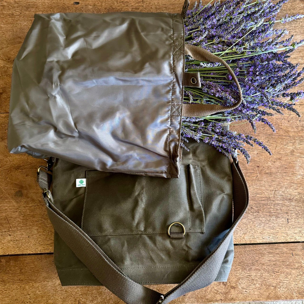 The Celtic Farm’s Gardeners Multipurpose Shoulder Bag in brown and olive green offers organized storage for tools, market finds, or harvests; both rest atop a wooden surface, one filled with fresh lavender sprigs.