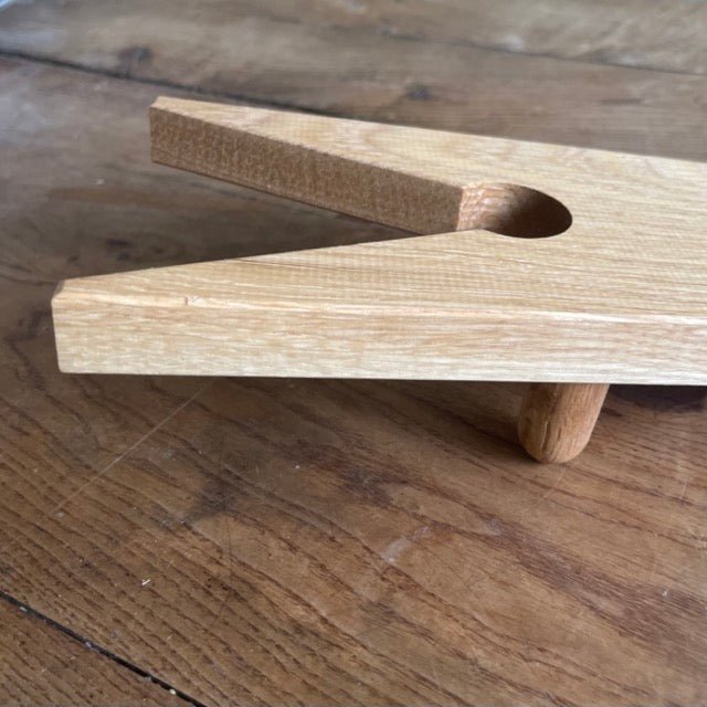 The Celtic Farm’s English Boot Jack - White Oak features a V-shaped notch and circular hole, handcrafted for easy removal of garden boots. Shown resting on wood, this rustic boot puller combines function with classic style.