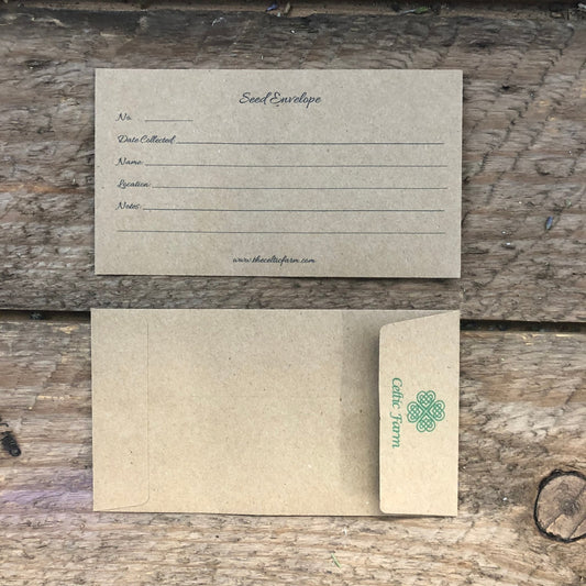Two brown Our Seed Envelopes/Packets from The Celtic Farm are shown on wood—one with collection fields, the other with a green clover logo—ideal for seed storage or as a thoughtful gift for gardeners.