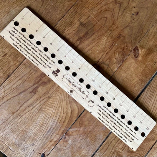 The Celtic Farm’s American Hardwood Seed and Bed Ruler, made in the US from American lumber, features measurement markings, evenly spaced holes in various sizes, and printed instructions—shown placed on a wooden table.