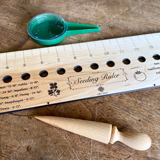 The Celtic Farm Seeding Gift Set - Dibble, Seeder and Ruler includes a wooden ruler, plastic seed dispenser, and dibber—essential tools for any gardener—all neatly arranged on a wooden surface.