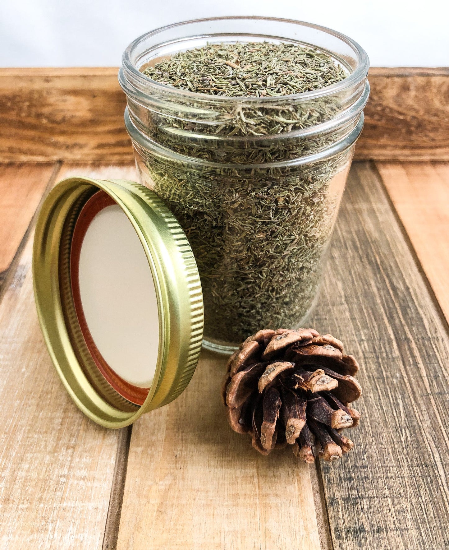 Small jar of dried thyme herbs in a herbalroseapothecary herb jar with wood and white design, ideal for kitchen storage or herbal remedies.