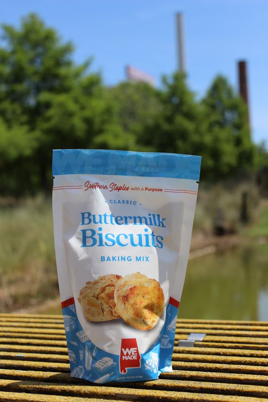 Bag of WE Made Buttermilk Biscuit Mix with a scoop of freshly baked biscuits on a rustic wooden surface.