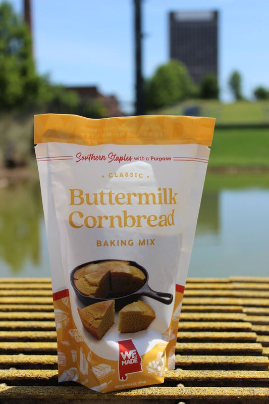 Box of WE Made Buttermilk Cornbread Mix with prepared cornbread slices on a plate, showcasing the baking mix and finished dish.