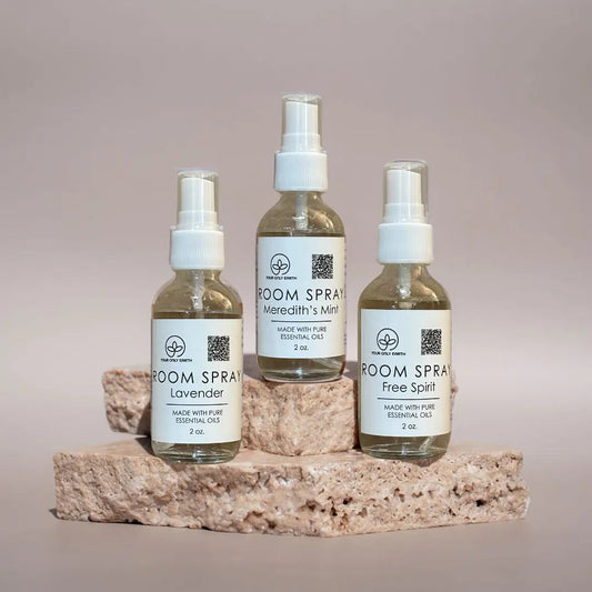 Three 2 oz Room Spray bottles from Your Only Earth, featuring Lavender, Merediths Mint, and Free Spirit scents, are elegantly displayed on a textured stone surface. Crafted with pure essential oils, they charm against a soft beige background—perfect for adding elegance and a natural touch.