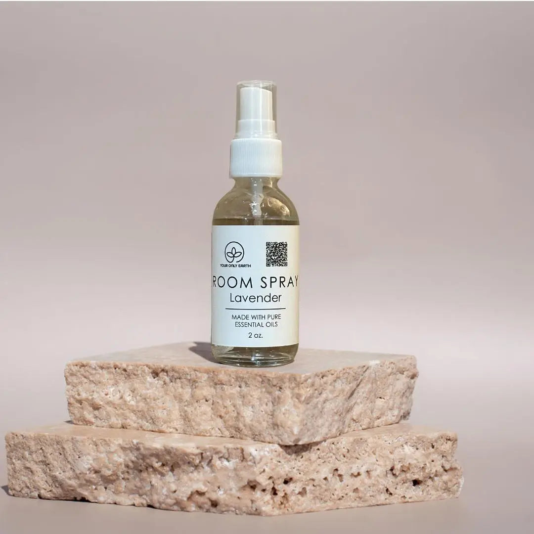 A 2 oz Room Spray bottle by Your Only Earth, made with pure essential oils, sits on two stone slabs against a neutral backdrop. Ideal for those who value the calming benefits of essential oils in room sprays.