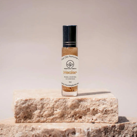 A Perfume Roll-on by Your Only Earth rests on a textured stone platform. Crafted with essential oils, it displays a logo and lists ingredients such as rose, lavender, and geranium. The background is a neutral, blurred gradient.