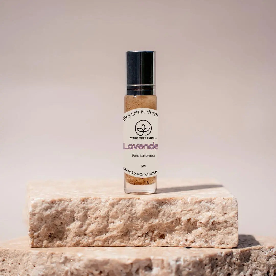 A small bottle of Perfume Roll-on rests on a textured stone platform. The label reads Lavender and Your Only Earth, hinting at luxurious essential oil blends, set against a soft, neutral background.