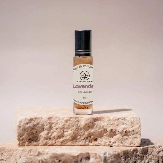 A small bottle of Perfume Roll-on rests on a textured stone platform. The label reads Lavender and Your Only Earth, hinting at luxurious essential oil blends, set against a soft, neutral background.