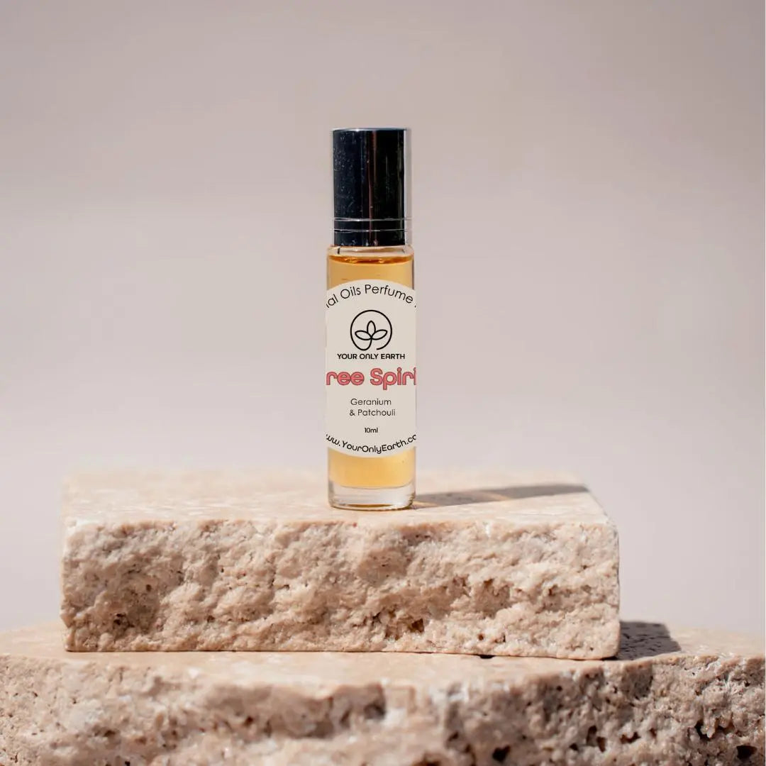 A small glass bottle of Perfume Roll-on by Your Only Earth with organic coconut oil rests on stacked stone tiles. Featuring geranium and patchouli scents, the neutral background conveys a natural, minimalistic vibe.