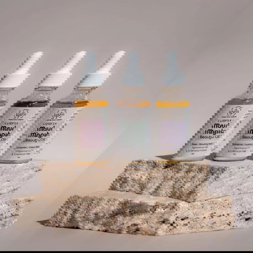A digitally distorted image shows Your Only Earth Maui Magic Beauty Oil dropper bottles on beige textured stones with glitch-like effects. Ideal for acne and rosacea, the scene features a neutral, softly lit background.