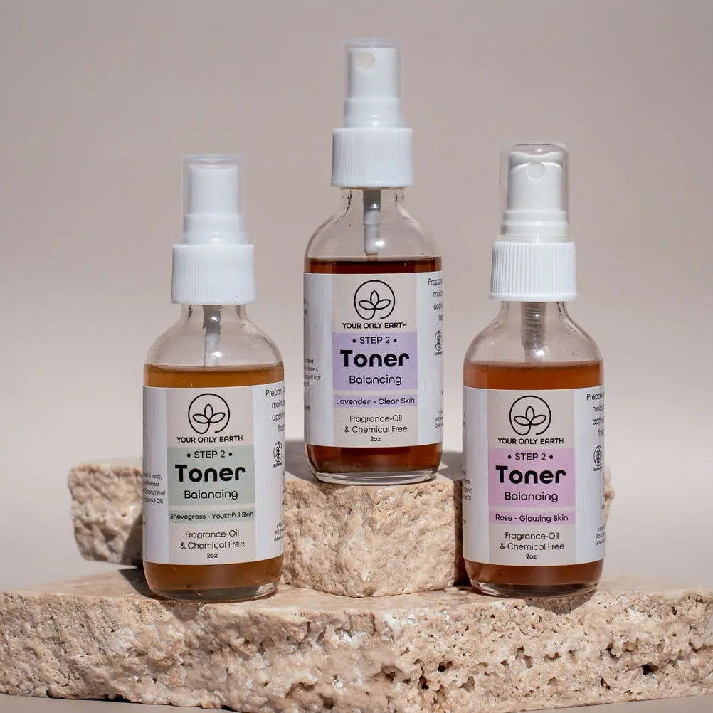 Three bottles of Your Only Earth Toner are shown on beige stone slabs. Their labels highlight that they are fragrance-free and chemical-free, making this hydrating toner ideal for natural skincare routines. The setting is neutral and well-lit.