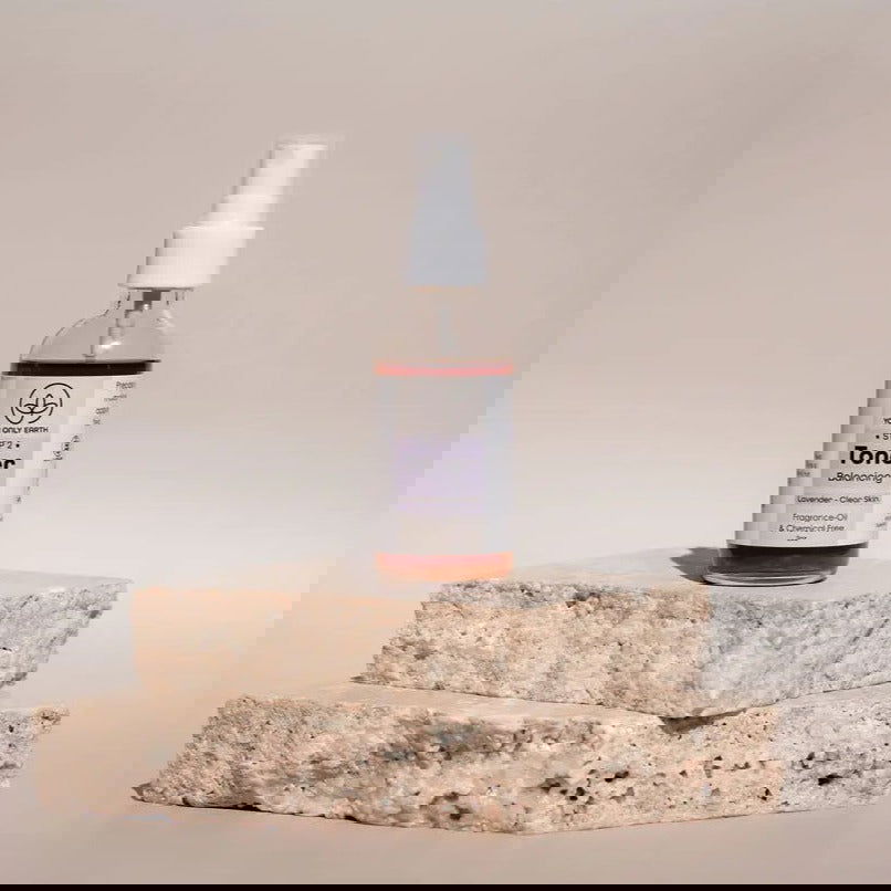 Two tubes of Your Only Earth Toner stand upright on rough stone slabs. Digital glitches distort the image, obscuring the labels and details against a plain, neutral background.