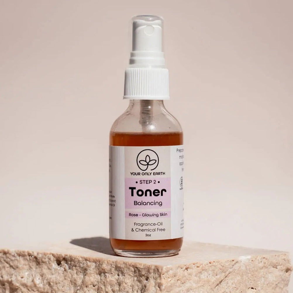 A 2 oz clear spray bottle of Your Only Earth Toner, fragrance-free and chemical-free, sits on a stone surface—this botanical toner promises rose-glowing skin for your natural skincare routine.