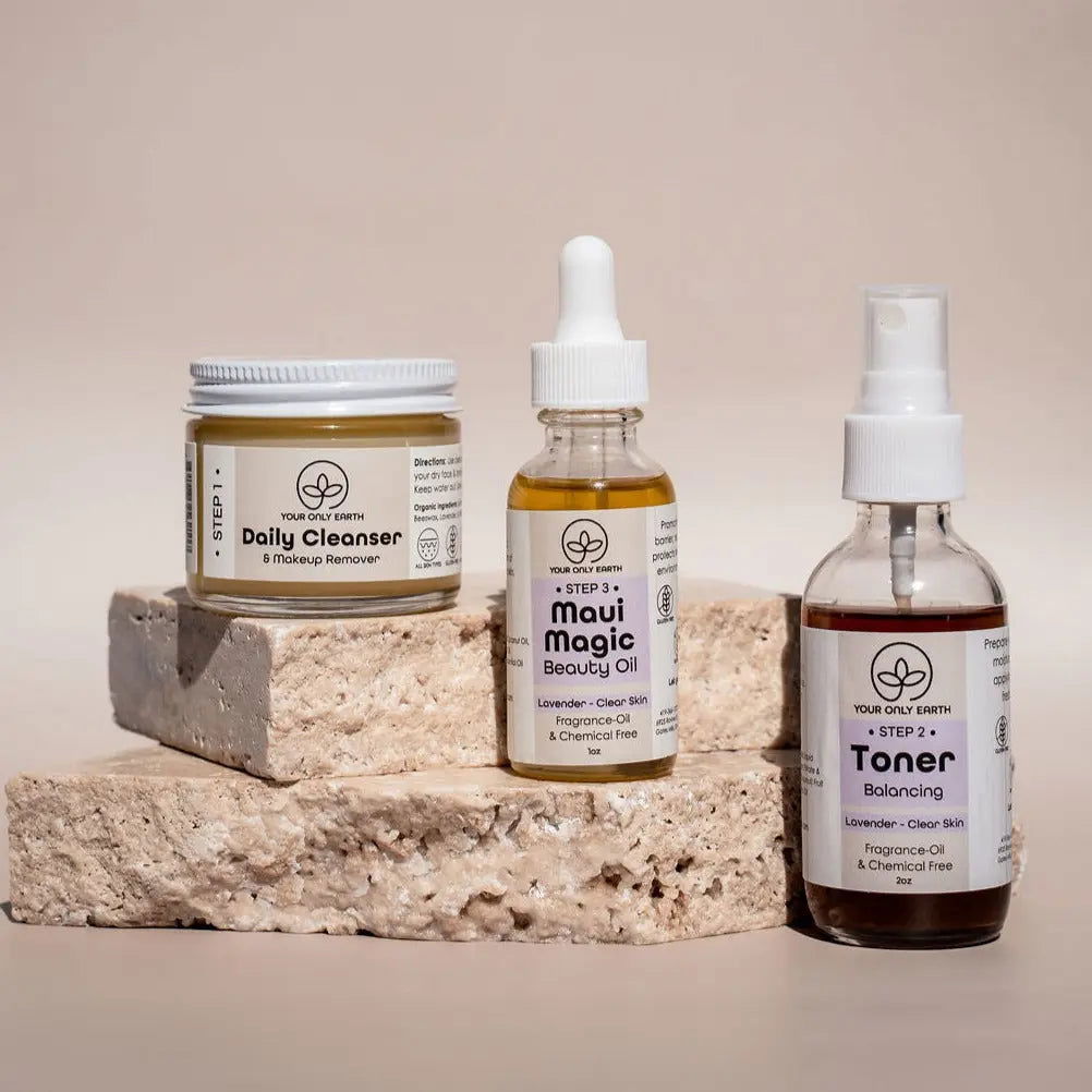 Three eco-friendly skincare essentials from Your Only Earth’s Dewy Skincare Set—a cleanser, beauty oil, and toner—sit on beige stone. Each label highlights plant extracts and natural, fragrance-free, chemical-free ingredients.