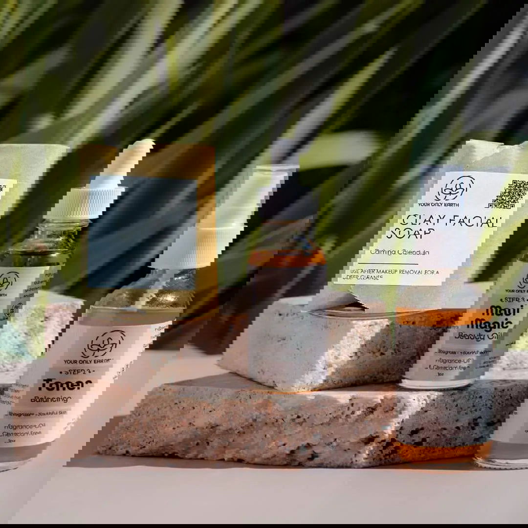 The Dewy Skincare Set by Your Only Earth is displayed in white bottles and boxes on stone blocks with green leaves casting shadows, creating a bright, minimalistic scene that highlights its plant extract-based, sustainable formula.