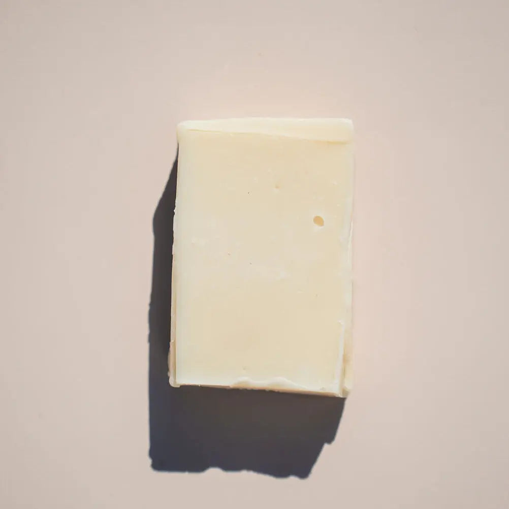 The creamy white Free Spirit Soap by Your Only Earth, exuding a subtle patchouli aroma, rests against a light beige background. It casts a soft shadow to the left, and its smooth surface with tiny imperfections enhances its natural hippie vibe.